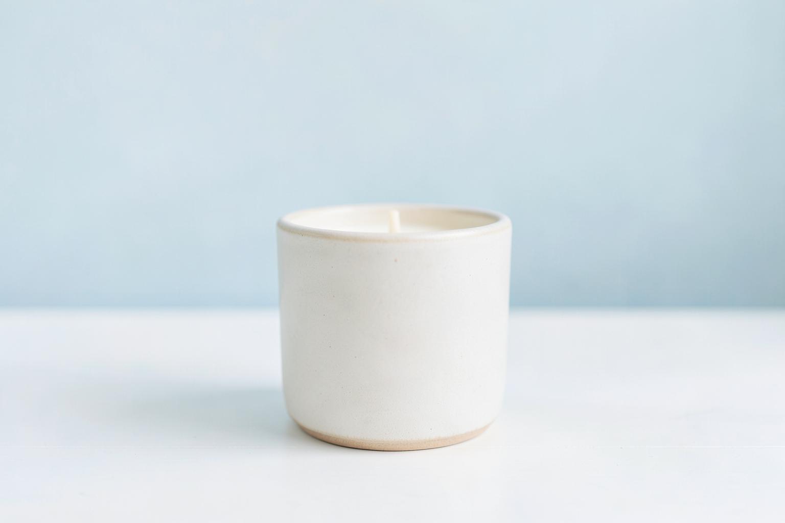 Hand-poured cream candle in a plain ceramic vessel on a pale blue background